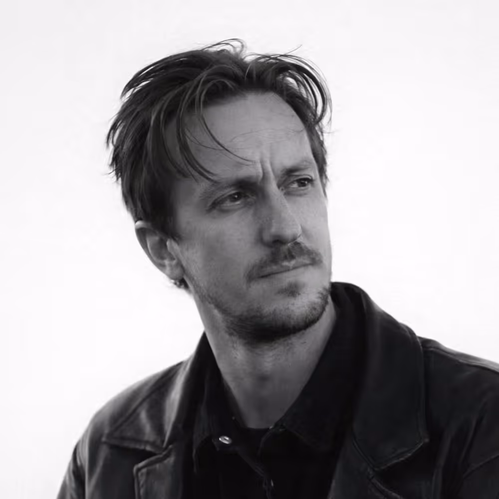 Black and white portrait of a man with tousled hair looking to the side wearing a leather jacket.